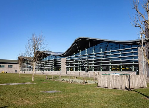 Modern building with wave-shaped roof and large glass windows under clear blue sky