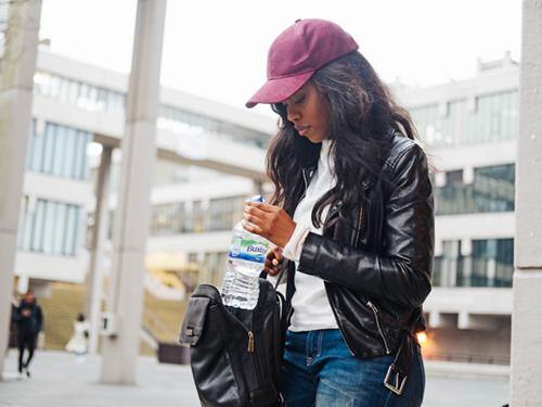 Woman keeping hydrated while commuting with a bottle of Buxton Water in her bag.