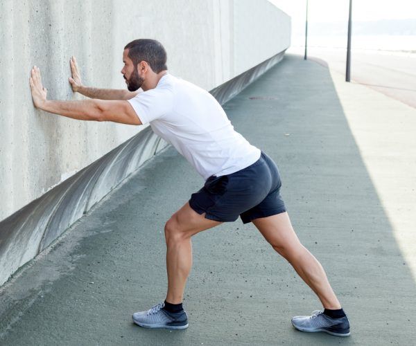 man leaning on a wall whilst stretching his calves.   