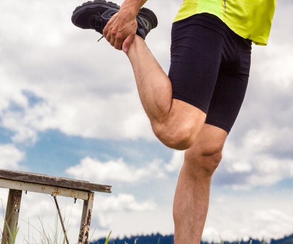 Man stretching his quadriceps before a run in a field.